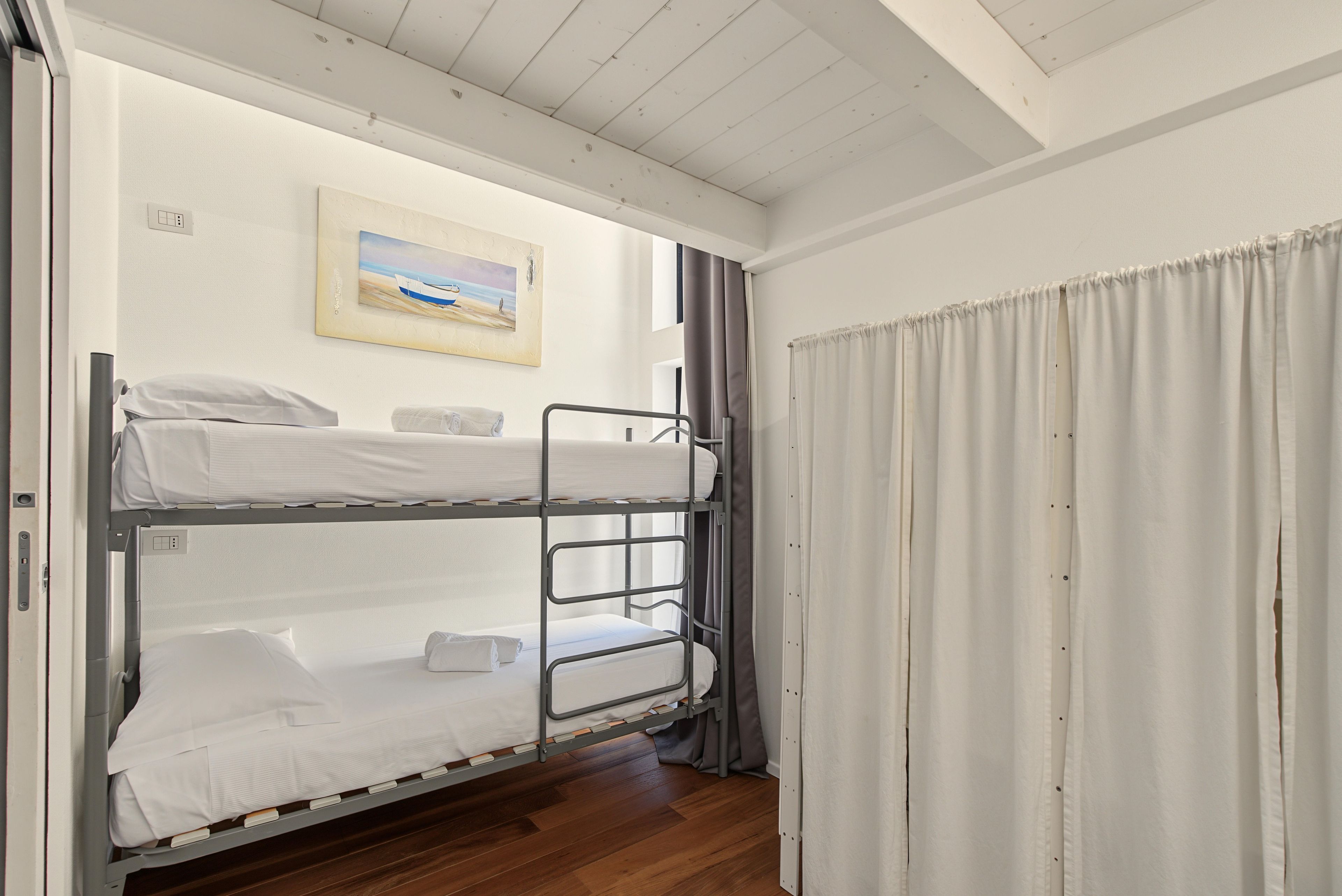 A bunk bed room with a painting on the wall and a curtain on the window.