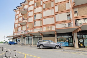 Un hotel de varios pisos con balcones, estacionamiento y un local comercial con señalización.