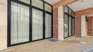 Facciata di un edificio con ampie porte e finestre in vetro, un muro in mattoni e un pavimento piastrellato.