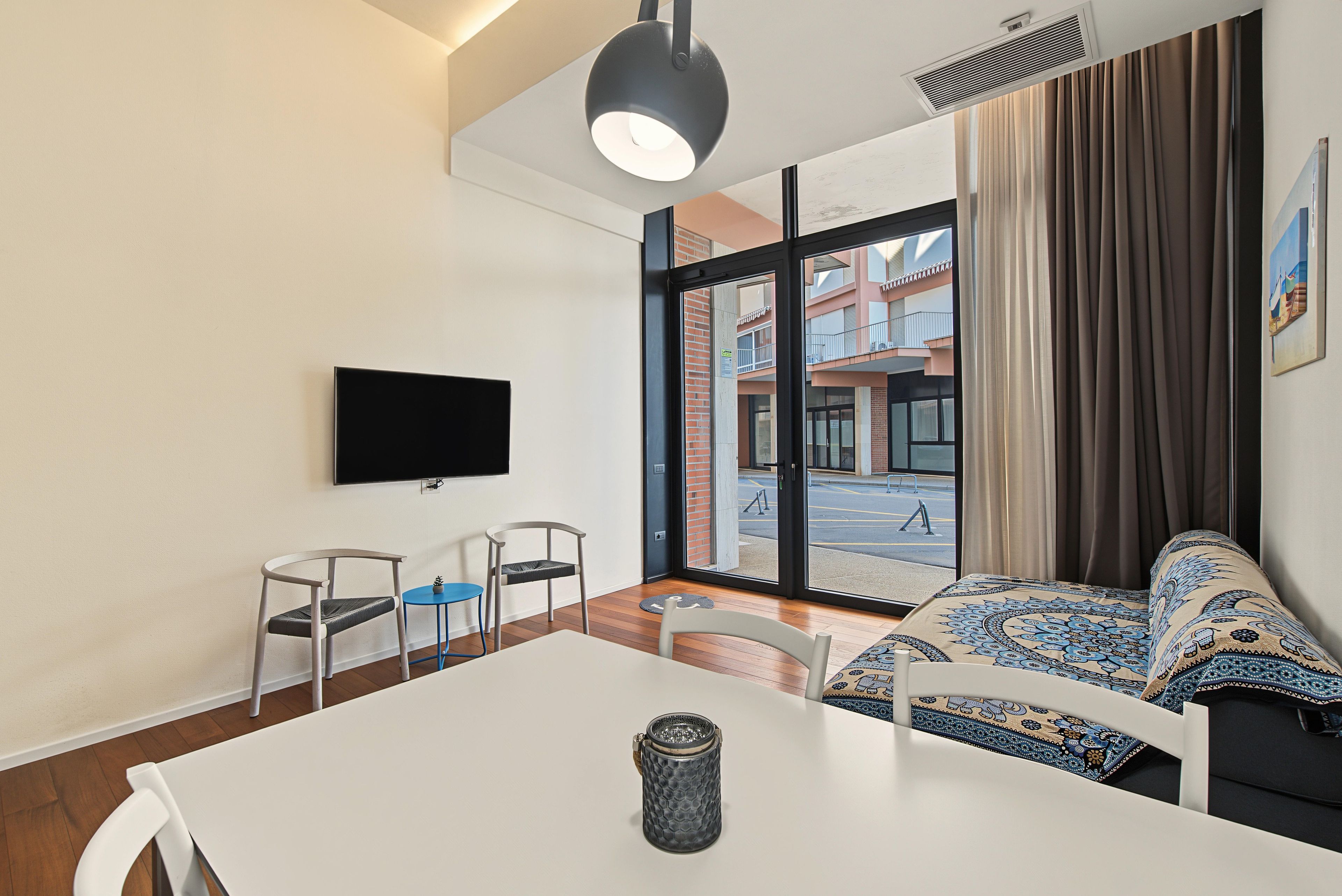 Une chambre d’hôtel moderne dotée d’une grande fenêtre, d’un téléviseur à écran plat, d’une table à manger et d’un canapé agrémenté de coussins à motifs.