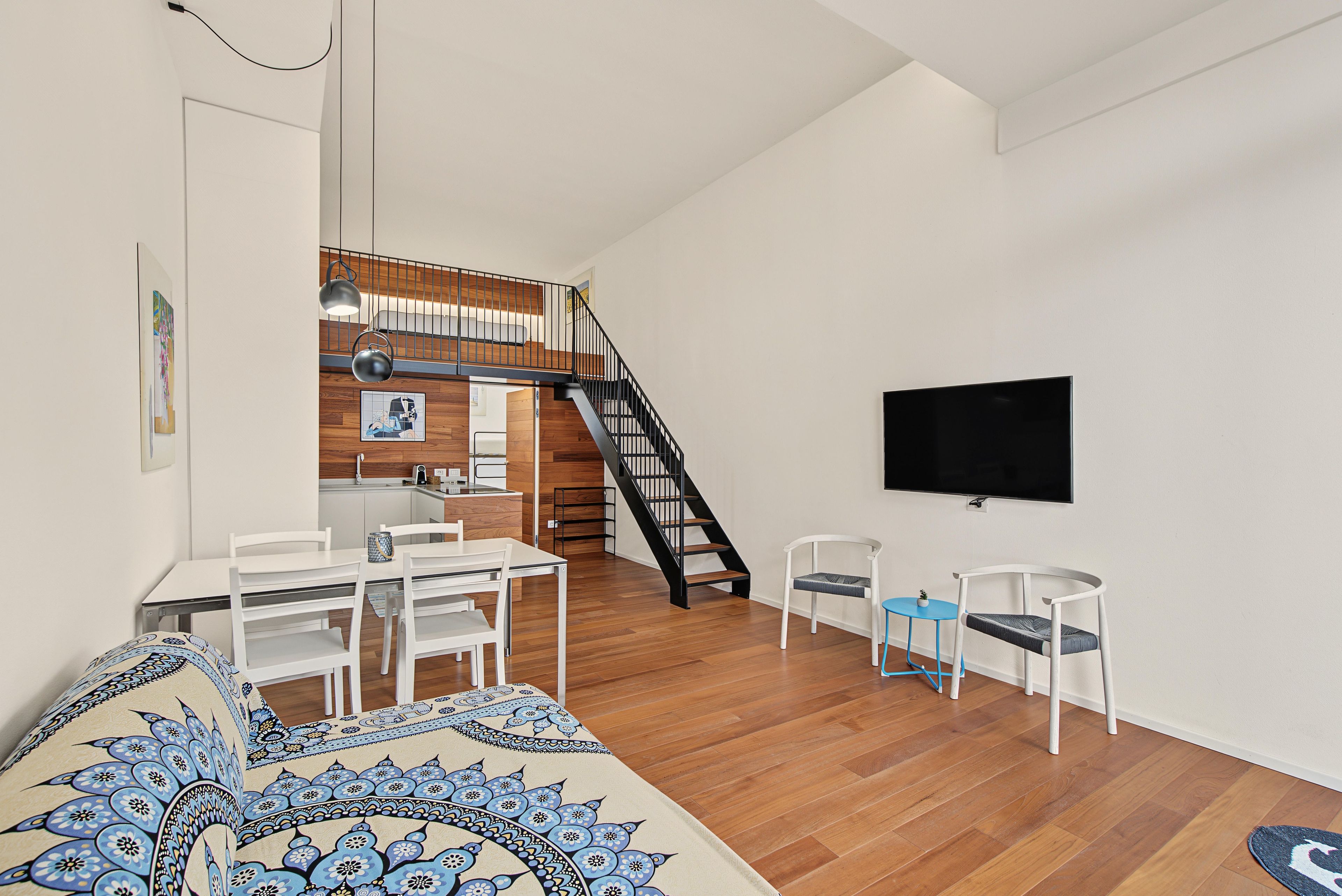 Una sala de estar moderna con un sofá, una mesa de comedor, sillas, un televisor y una escalera.