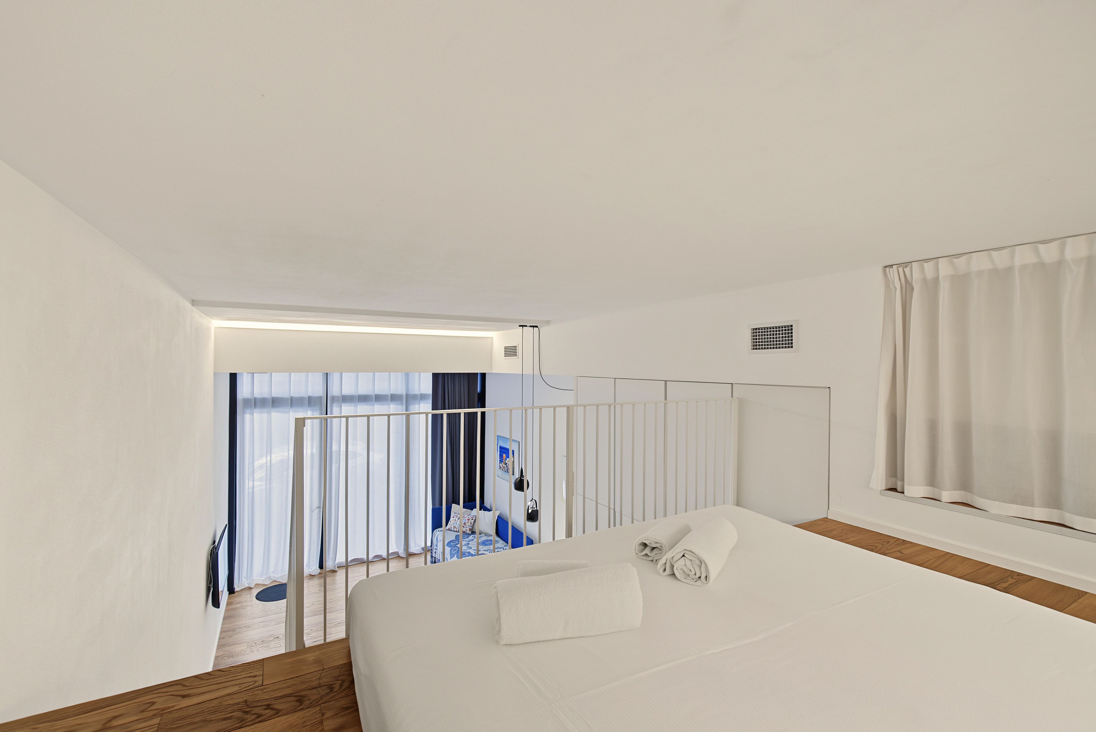 A modern hotel room with a large bed, a view of the balcony, and a window with curtains.
