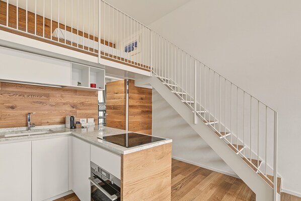 A modern kitchen with a built-in oven, a wooden accent wall, and a white staircase leading to an upper level.