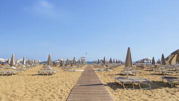 Een strand met een houten looppad naar de zee, omzoomd met ligbedden en parasols.