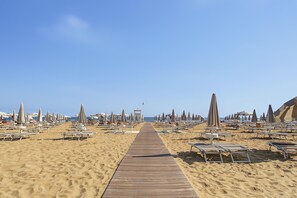 A beach with a wooden walkway leading to the sea, lined with sun loungers and umbrellas.