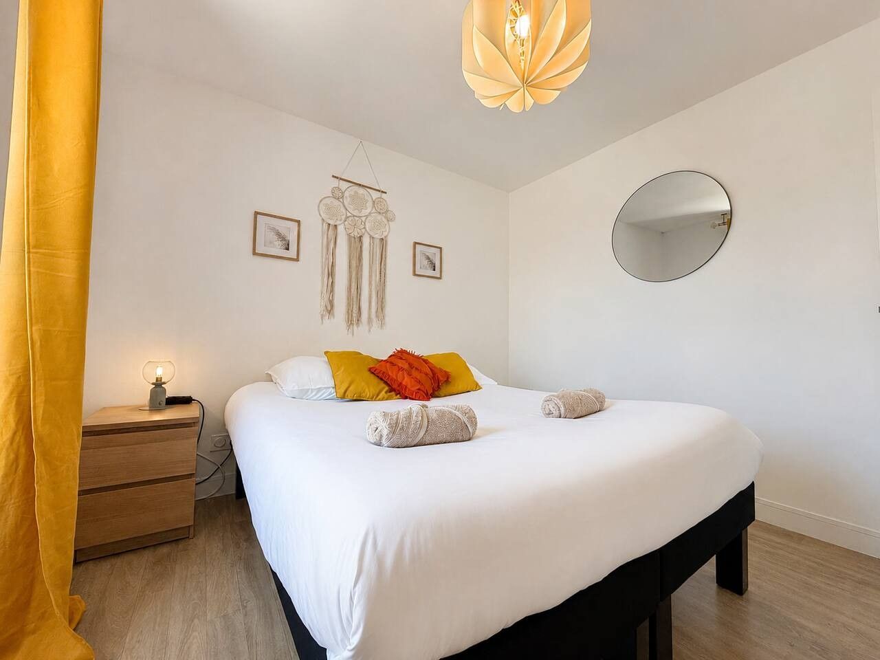 A bedroom with a bed, bedside table, lamp, wall decor, and a mirror.