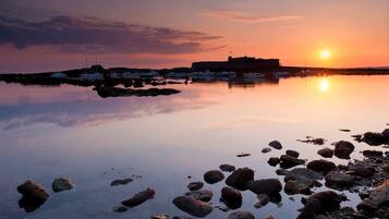A calm waterfront with boats, a rocky shoreline, and a distant building.