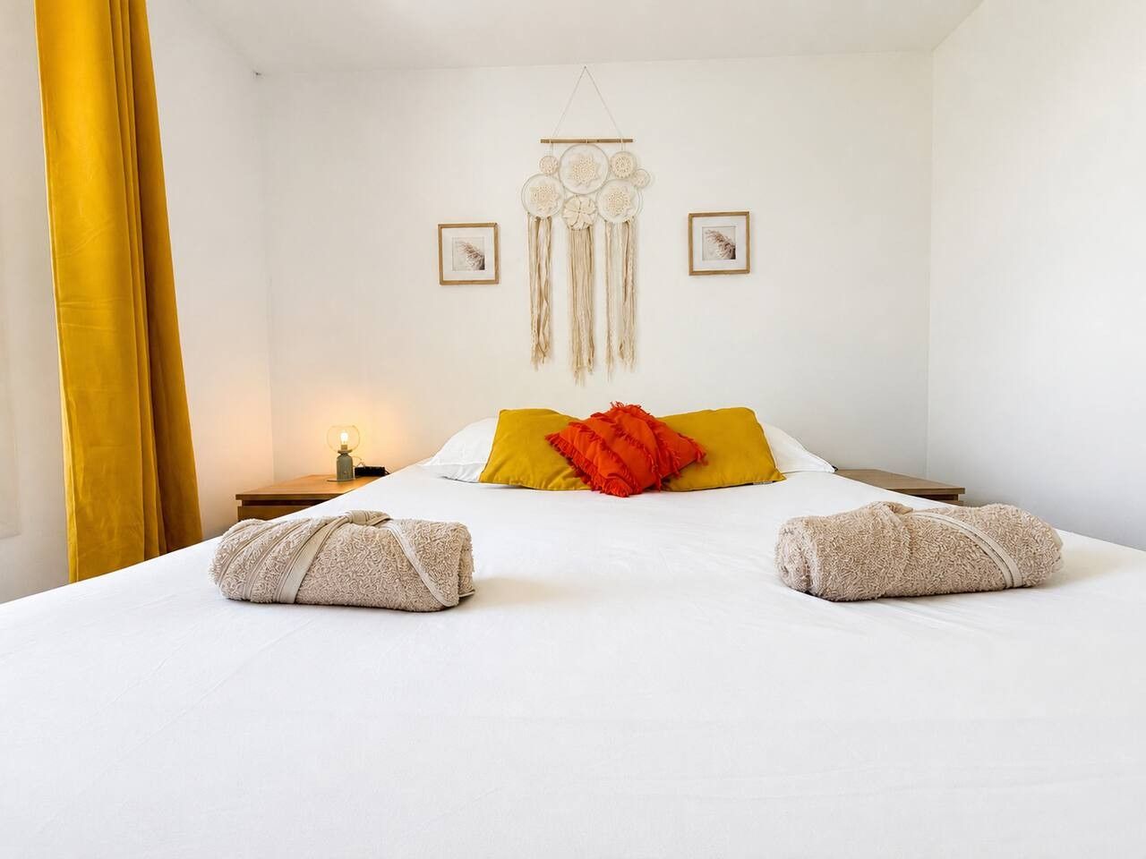 A hotel room with a bed, a decorative wall hanging, and two framed pictures.