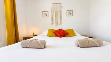 A hotel room with a bed, a decorative wall hanging, and two framed pictures.