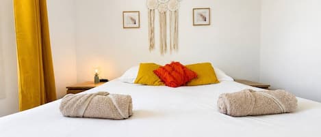 A hotel room with a bed, a decorative wall hanging, and two framed pictures.