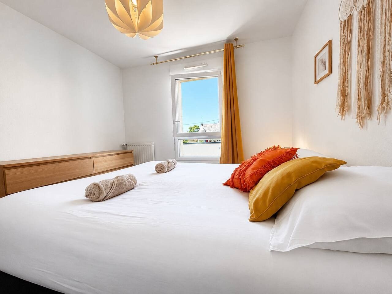 Een hotelkamer met een bed, een houten hoofdeinde, een raam met gordijnen en uitzicht op buiten.