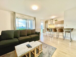 A modern living room with a sofa, a coffee table, and a dining area with chairs. - L'atelier Chic - Balcony, Netflix, Parking, 2-room apartment (Lanester)