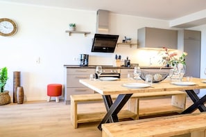 Eine moderne Küche mit einem Holzespeisetisch, gedeckt für vier Personen, einem eingebauten Backofen und einem flachbildfernseher, der über der Arbeitsplatte angebracht ist.