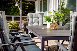 Ein Sitzbereich im Freien mit Tisch und Stühlen, einem Blumentopf und Blick ins Grüne.