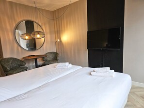 A hotel room with a large bed, two armchairs, a small table, a round mirror, and a flat-screen TV. - Studio Zoet Do46 Domburg (Domburg)