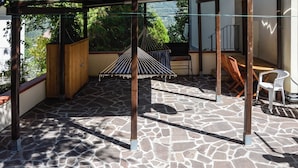 A stone-tiled patio with a hammock, wooden furniture, and a view of greenery. - Tavernetta Openspace (Sparvo)