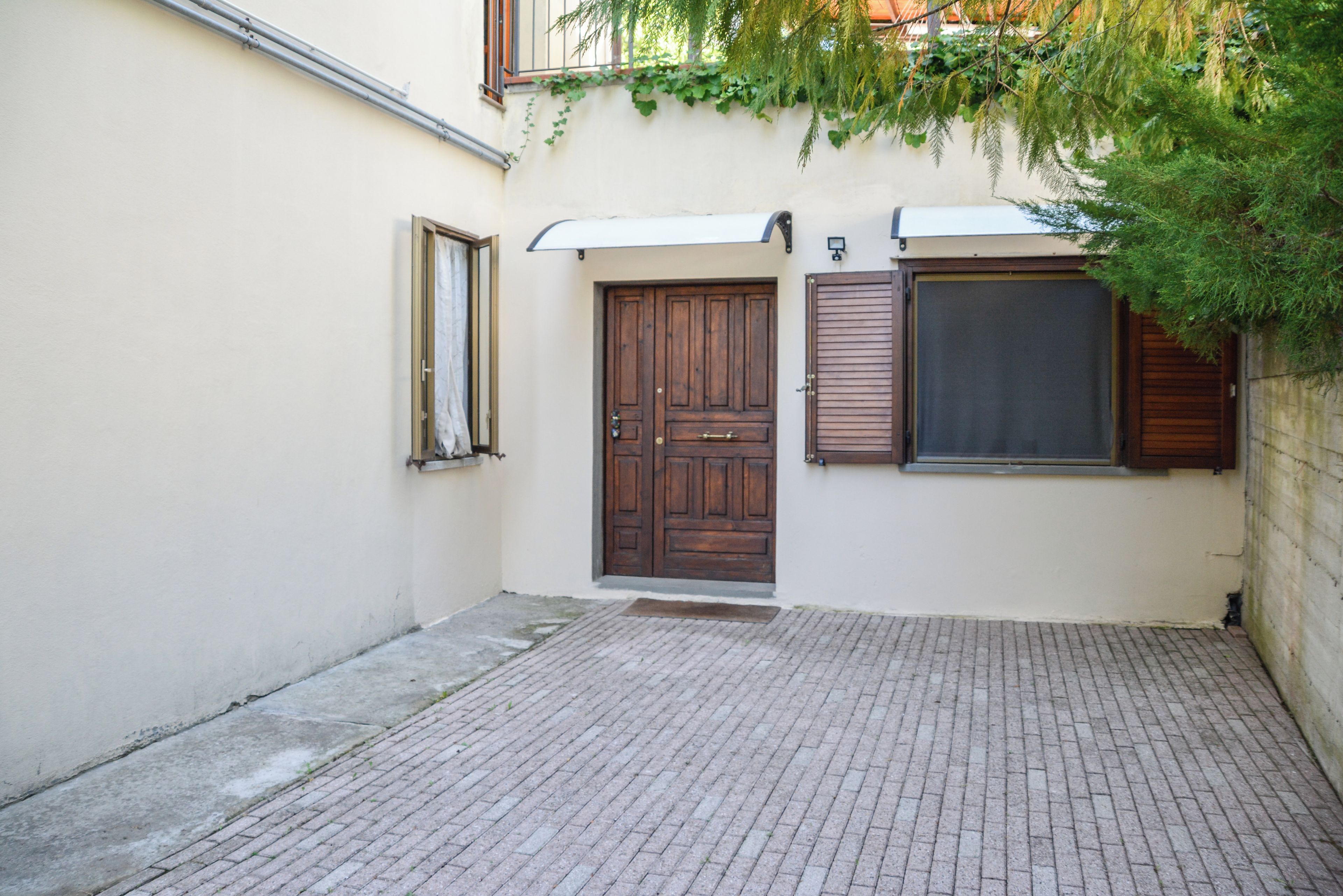 Un estrecho callejón con pavimento de ladrillo, una puerta de madera y una ventana con contraventanas.