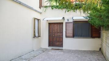 Un estrecho callejón con pavimento de ladrillo, una puerta de madera y una ventana con contraventanas.