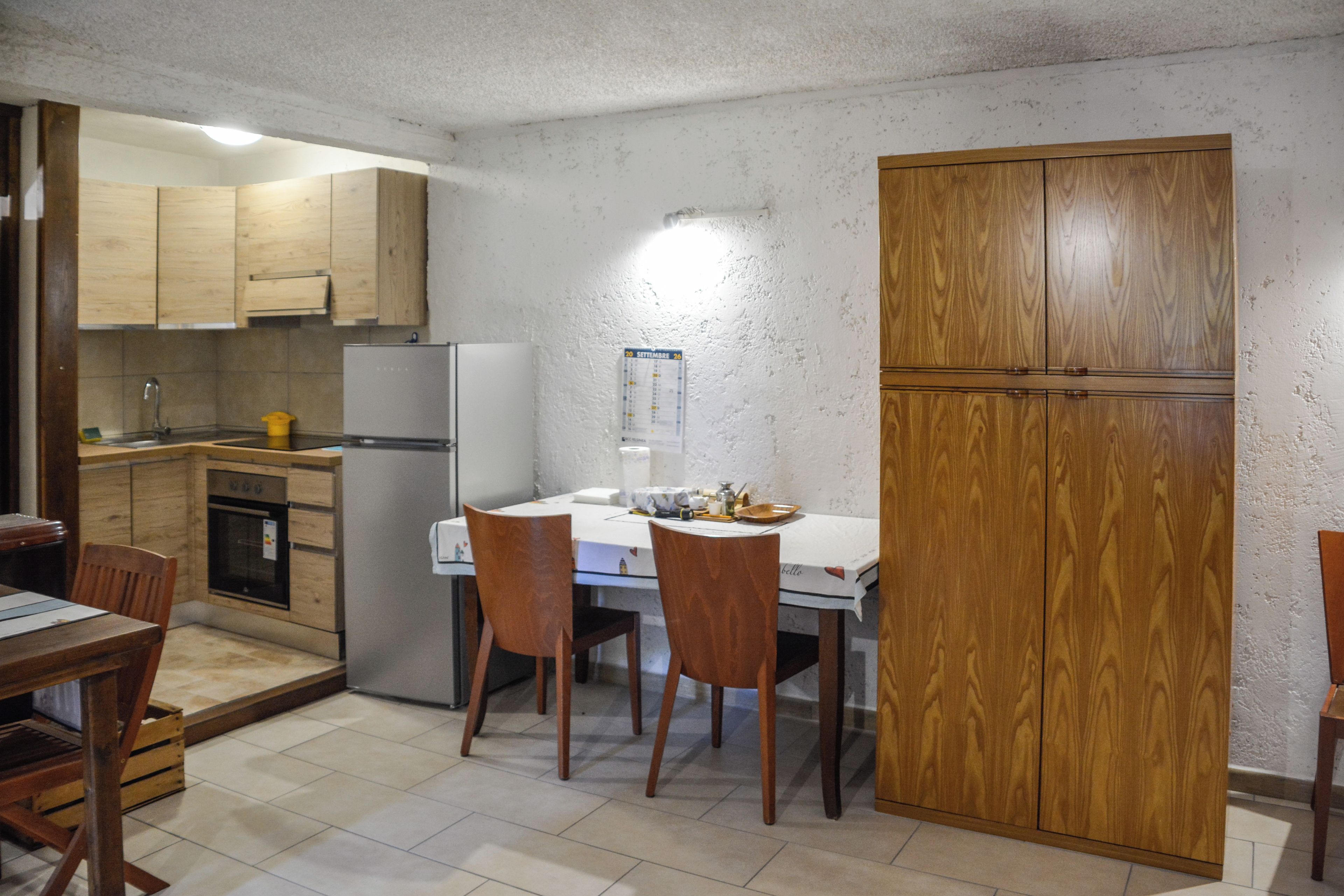 Cocina compacta con armarios de madera, un refrigerador y una mesa de comedor con sillas.