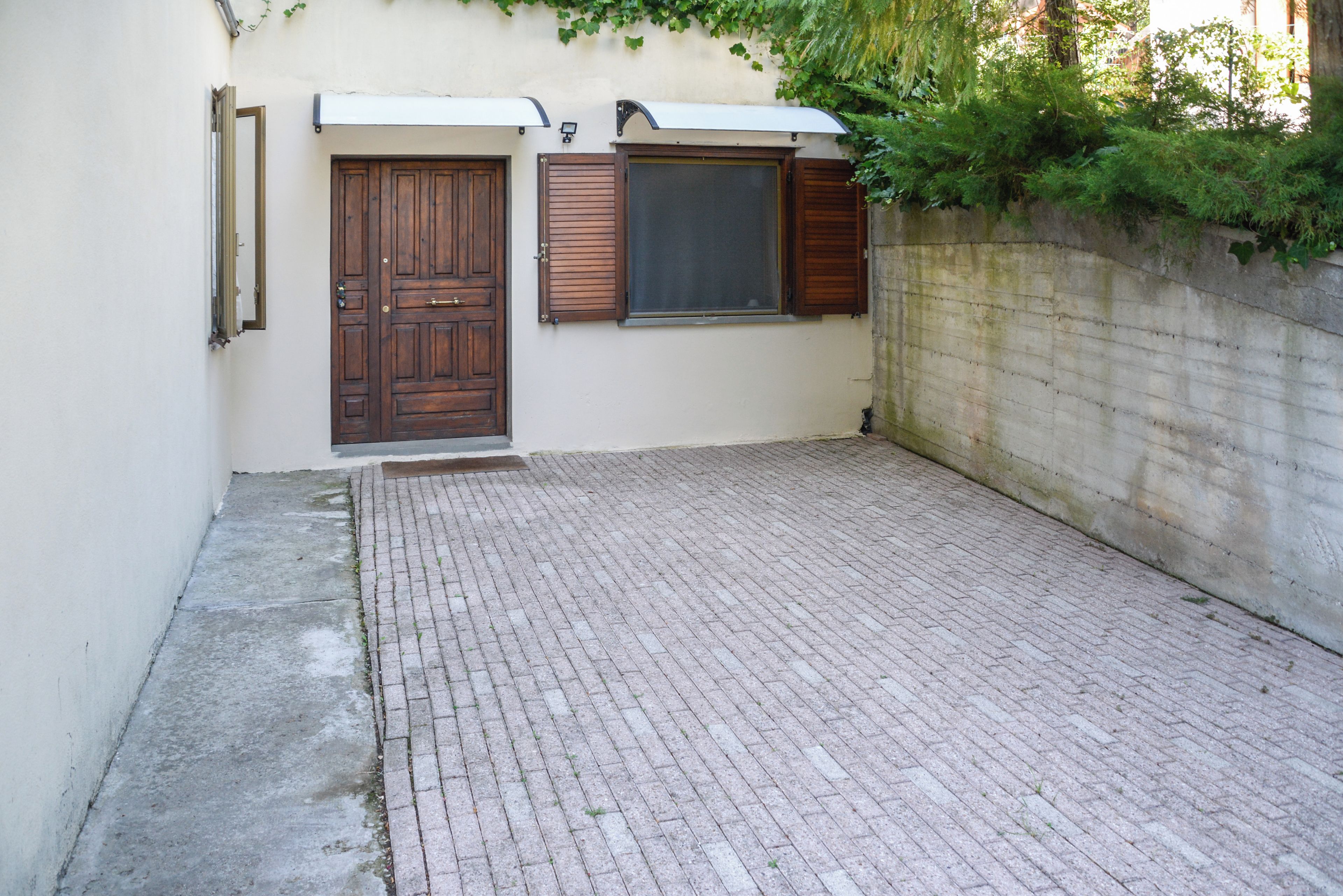 A paved courtyard with a brick floor, two wooden doors, and a window with shutters.