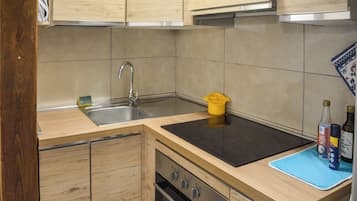 A kitchen with wooden cabinets, a stainless steel sink, a black countertop, and a blue mat.