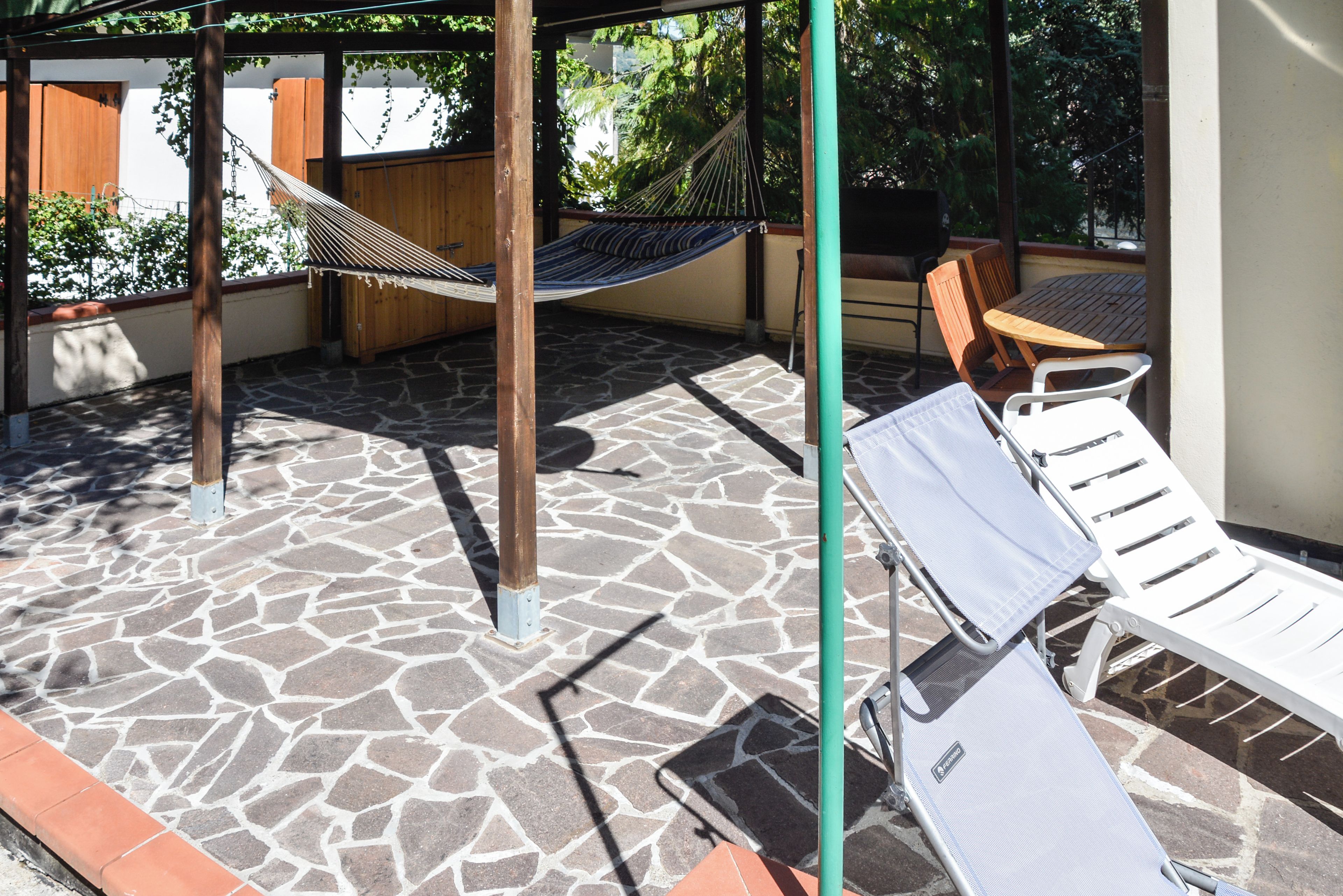 A patio with a hammock, a wooden table, and a white lounge chair.