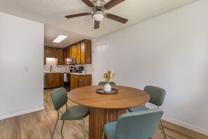 Un'area pranzo con un tavolo rotondo in legno, quattro sedie e una ventola a soffitto.