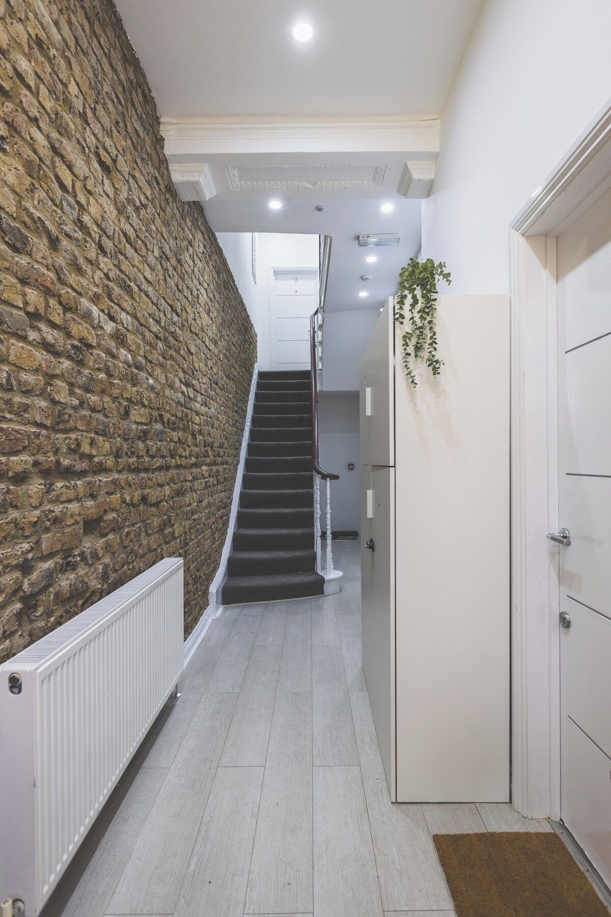 A narrow hallway with a stone wall on one side, a staircase leading to an upper floor, and a white door on the right.