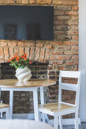 Eine Ziegelwand mit einem flachbildfernseher, der über einem Holztisch mit einer weißen Blumenvase angebracht ist.