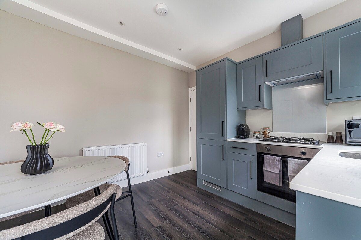 A modern kitchen with grey cabinets, a white countertop, and a dining area with a table and chairs.
