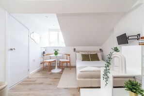 A compact living space with a bed, a small table with chairs, a washing machine, and a television mounted on the wall. - Contemporary Studio with Parking, Finsbury Park (Greater London)