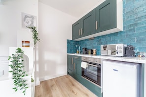 A compact kitchen with teal cabinets, a white countertop, and a small refrigerator. - Contemporary Studio with Parking, Finsbury Park (Greater London)