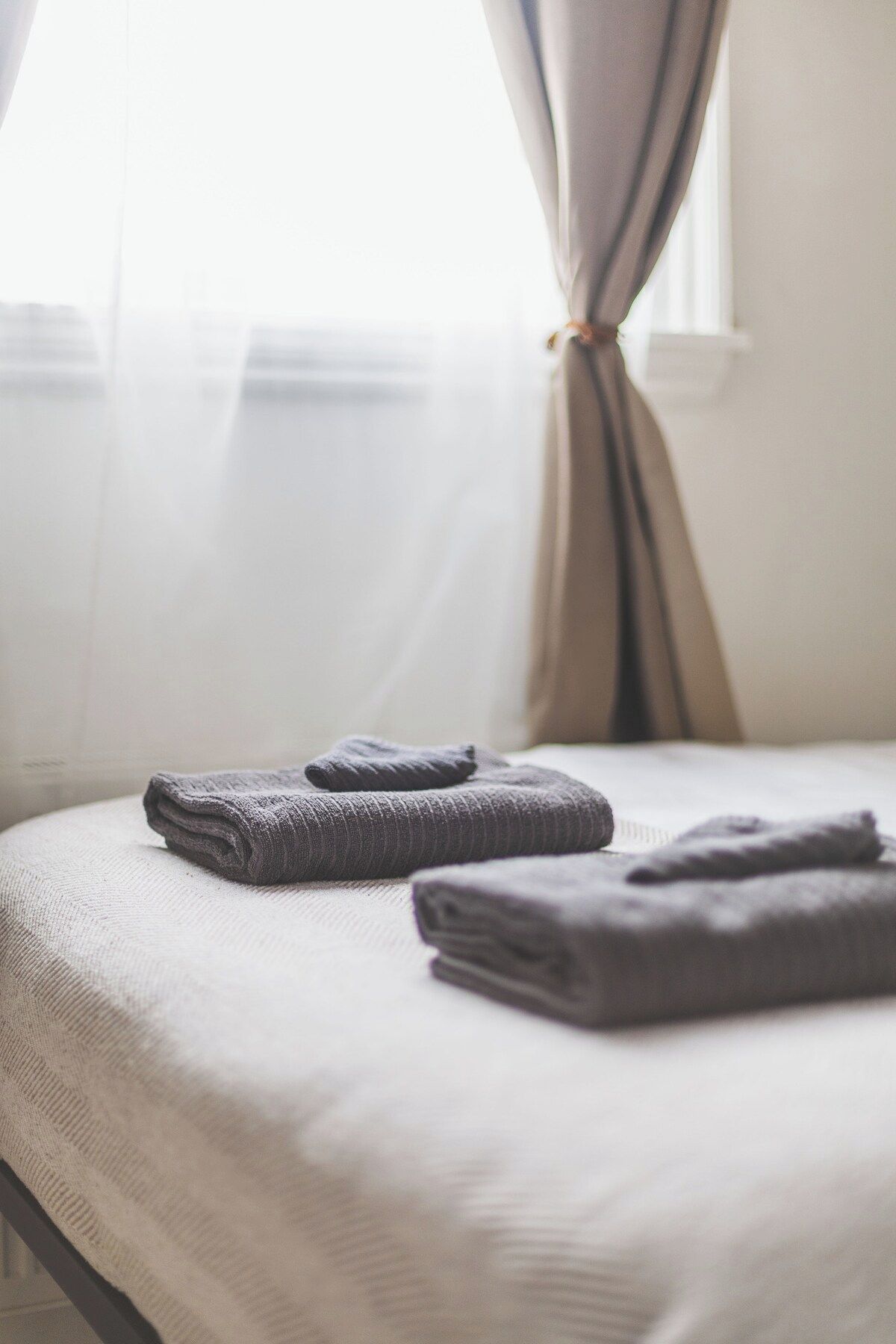 Een net opgemaakt bed met opgevouwen handdoeken en een raam met dunne gordijnen.