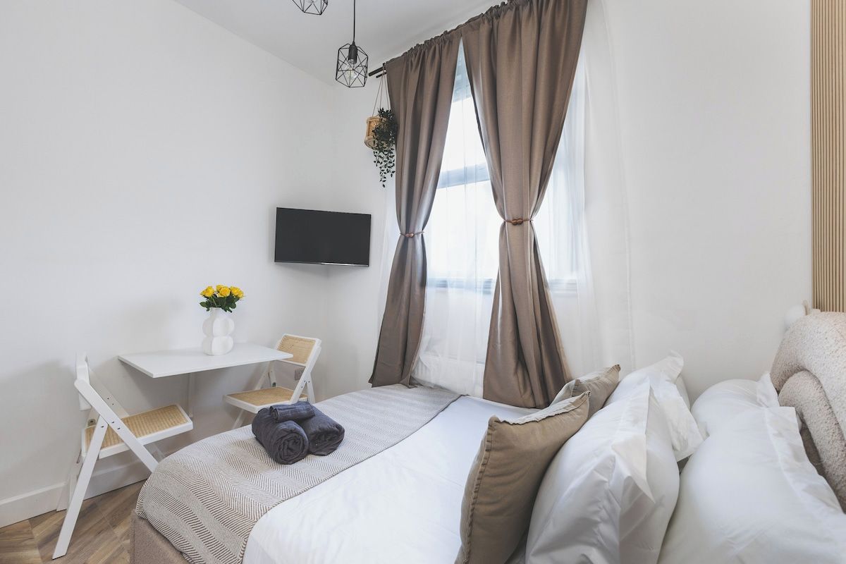 Ein Hotelzimmer mit einem Bett, einem Schreibtisch, einem Sessel, einem Fernseher und einem Fenster mit Vorhängen.