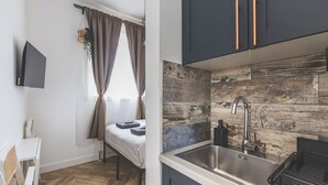 Cozinha compacta com design moderno, destacando um painel de madeira, uma pia de aço inoxidável e armários escuros com puxadores de cobre.