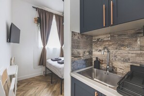 A compact kitchen with a modern design, featuring a wooden backsplash, a stainless steel sink, and dark cabinetry with copper handles. - Stylish cosy studio - Arsenal 15 min walk 01 (Greater London)