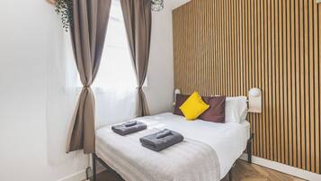 A modern bedroom with a bed, curtains, a wall-mounted lamp, and a wooden panel wall.