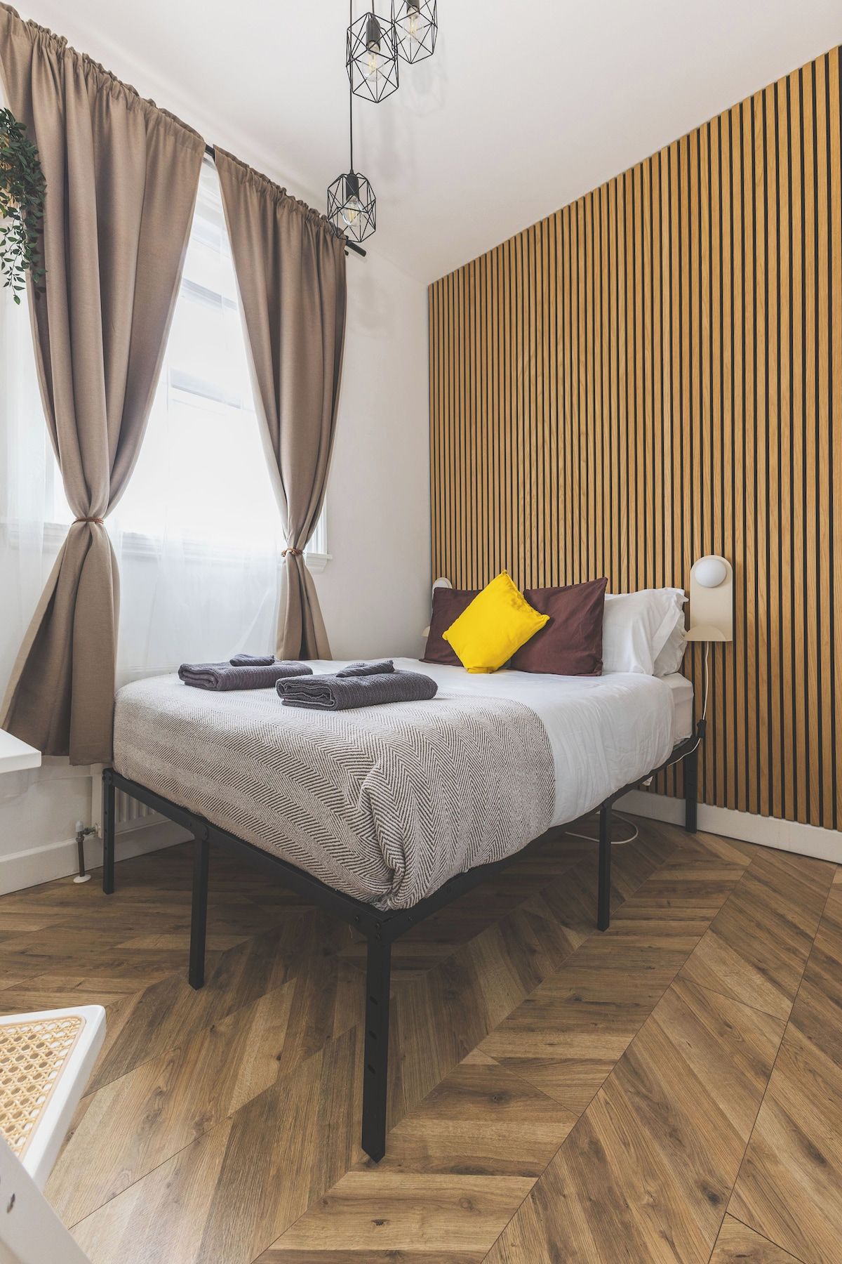 A modern bedroom with a bed, wooden panel wall, and a herringbone floor pattern.