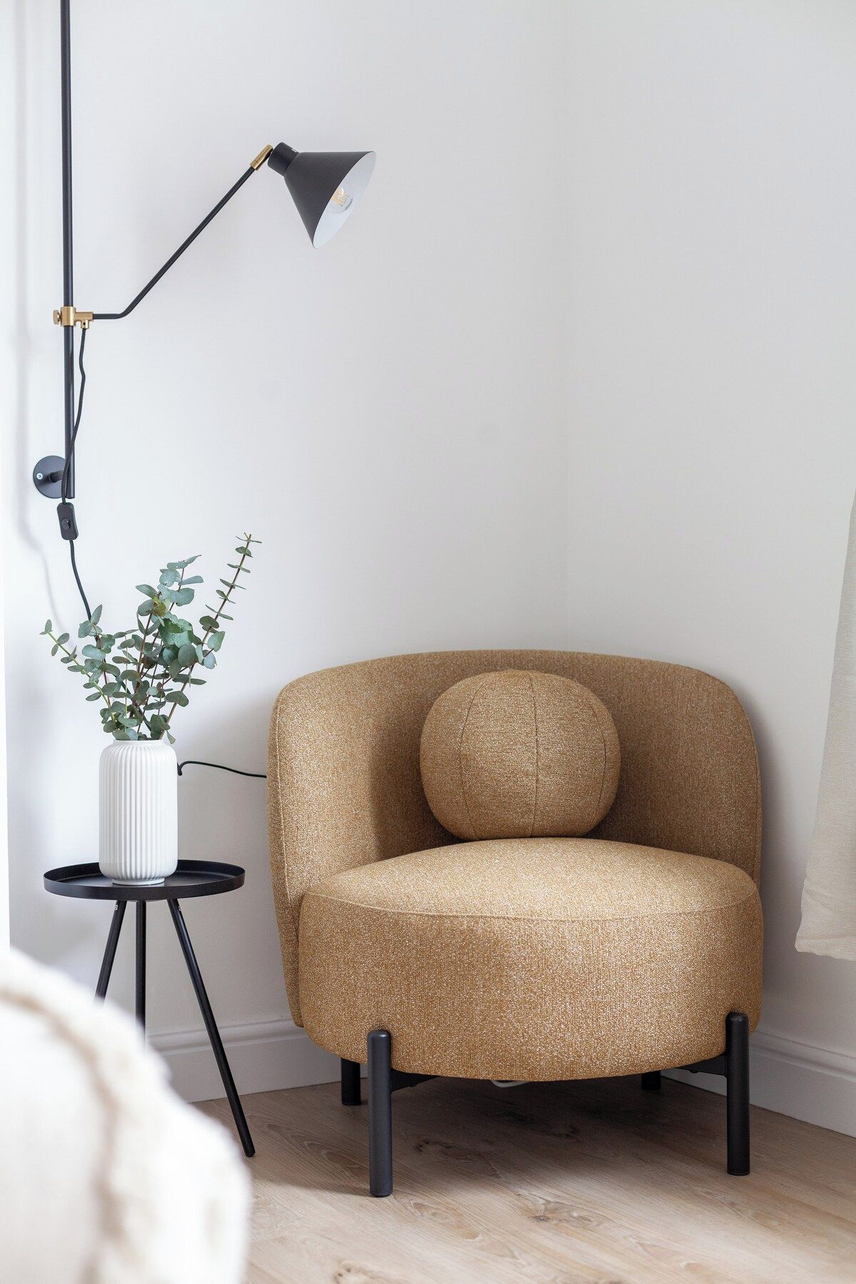 A room with a single armchair, a floor lamp, and a small table with a potted plant.