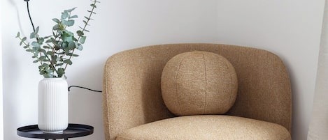 A room with a single armchair, a floor lamp, and a small table with a potted plant.