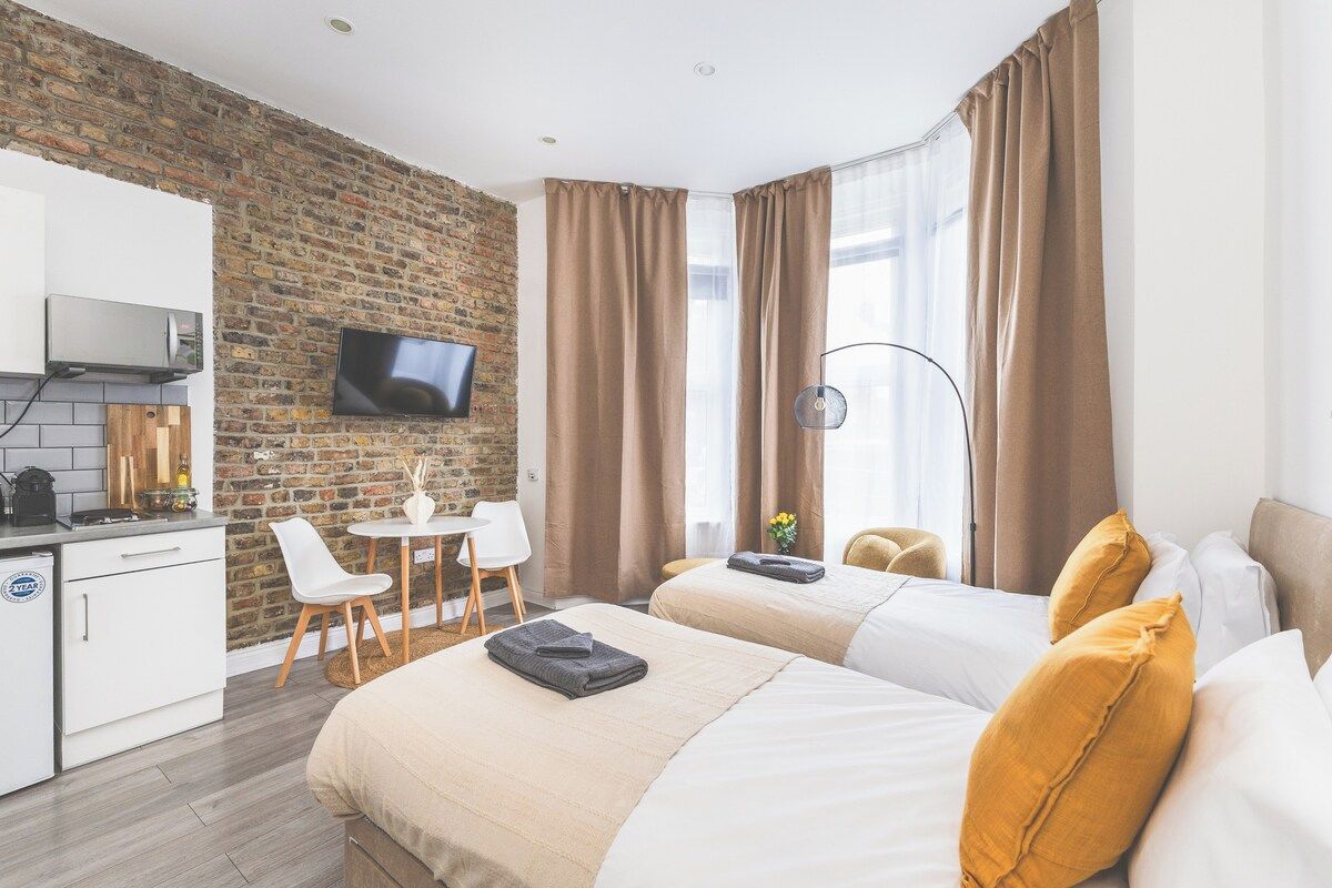 Une chambre d’hôtel avec un mur en briques, un téléviseur à écran plat, une kitchenette, deux lits et une fenêtre avec des rideaux.