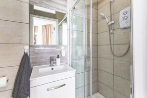 A modern bathroom with a glass shower enclosure, a white sink, and a mirror above it. - Lovely Studio Flat in Kilburn w/great location (Greater London)