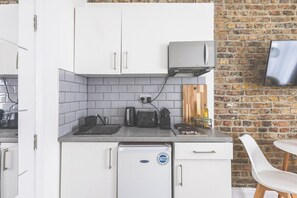 A compact kitchen with white cabinets, a built-in toaster, and a small refrigerator. - Lovely Studio Flat in Kilburn w/great location (Greater London)