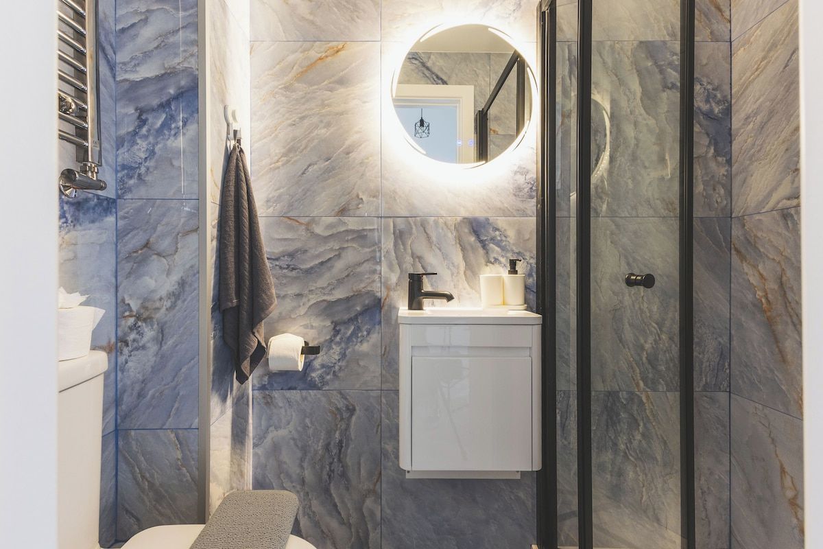 A bathroom with a marble wall, a round mirror, a sink, and a toilet.