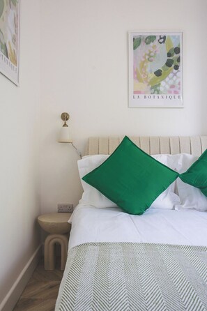 A bedroom with a bed, pillows, a nightstand, a lamp, and a wall art piece. - Large Studio Flat - Highbury Great Location (Greater London)