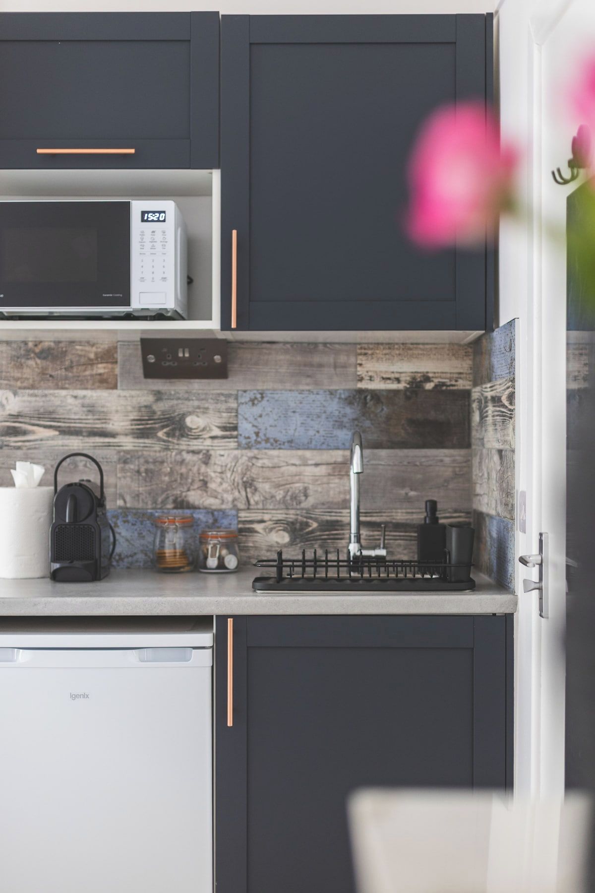 Een moderne keuken met donkere kastjes, een witte magnetron, een koffieapparaat en een landelijke spatwand.