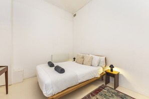 Ein schlichter Schlafzimmer mit einem Einzelbett, einem kleinen Nachttisch mit Lampe und einem gemusterten Teppich.