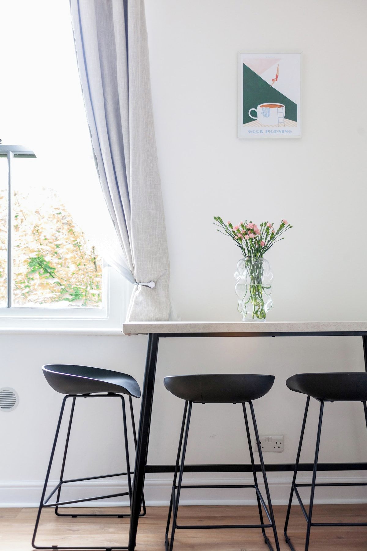 A kitchen with a window, a vase with flowers, and a framed picture on the wall.