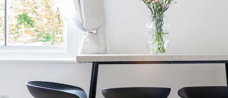 A kitchen with a window, a vase with flowers, and a framed picture on the wall.
