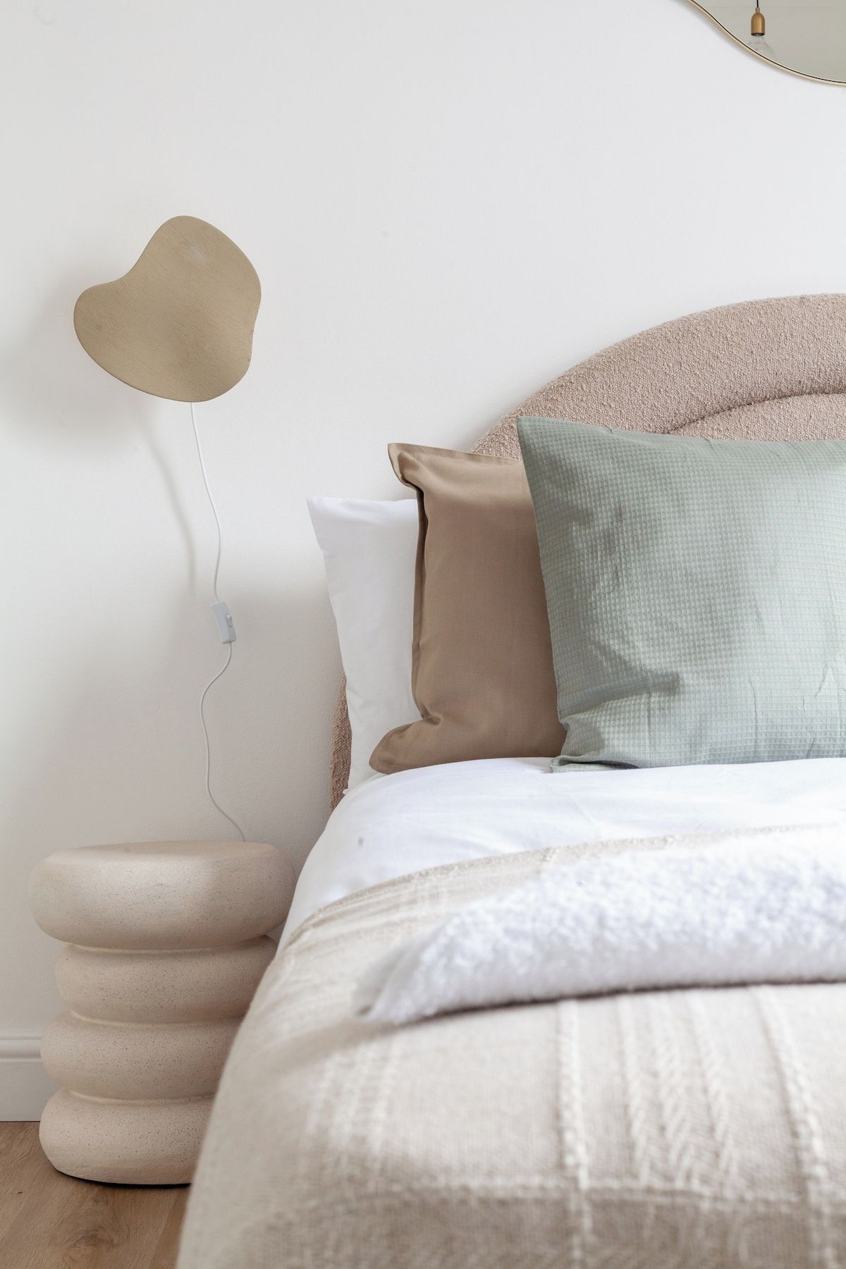 A neatly arranged bedroom with a bed, pillows, and a wall-mounted light fixture.